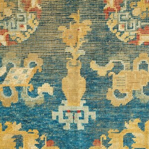 May include: Close-up of a blue and yellow patterned rug with intricate designs. The rug has a faded, vintage look and features a repeating pattern of floral motifs.