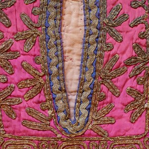 May include: Close-up of a pink fabric with intricate gold embroidery. The embroidery features a repeating pattern of leaves and swirls.