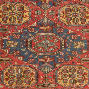 Puede incluir: Primer plano de una alfombra estampada en rojo, azul y amarillo. La alfombra presenta formas geométricas y motivos florales. El diseño central es un octágono azul con un centro rojo y amarillo. La alfombra tiene un estilo oriental tradicional.