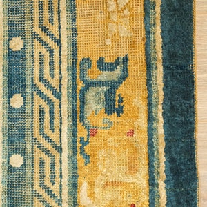 May include: Close-up of a blue and yellow rug with a geometric pattern. The rug has a fringe border and is made of wool.