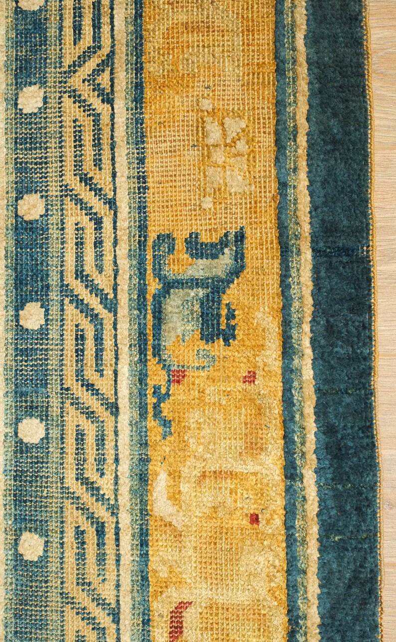 May include: Close-up of a blue and yellow rug with a geometric pattern. The rug has a fringe border and is made of wool.