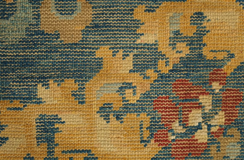 May include: Close-up of a woven tapestry with a blue, red, and yellow floral pattern.