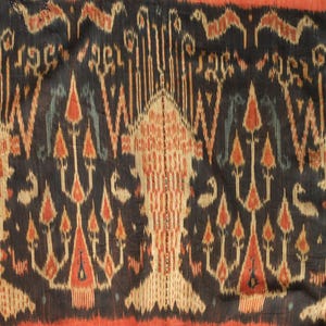 Könnte beinhalten: Textil mit einem sich wiederholenden Muster in Schwarz, Beige, Rot und Blau. Das Design zeigt stilisierte baumartige Formen und geometrische Elemente. Der Stoff hat ein strukturiertes Aussehen, mit einem roten Rand unten.