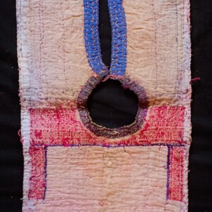 May include: A pink and white quilted fabric panel with a blue and white embroidered design. The panel has a round hole in the center and is edged with pink and red fabric.