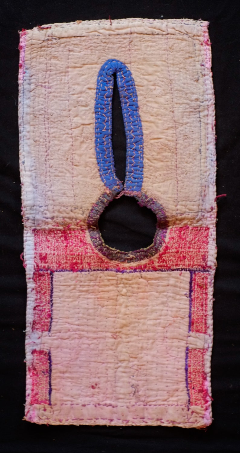 May include: A pink and white quilted fabric panel with a blue and white embroidered design. The panel has a round hole in the center and is edged with pink and red fabric.