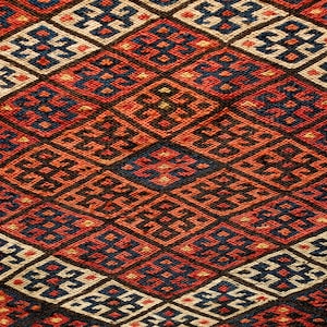 May include: A close-up of a red, blue, and white patterned rug with a geometric design. The rug is woven with intricate details and has a traditional look.