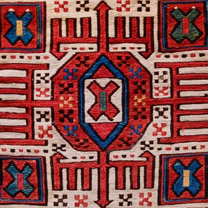 May include: A white rug with a red, blue and green geometric pattern. The pattern is symmetrical and features a central diamond shape.