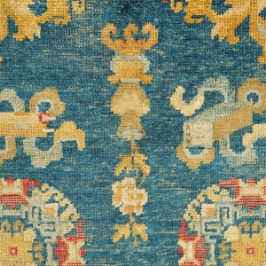 May include: Close-up of a blue rug with intricate patterns in shades of yellow, red, and white. The rug features a repeating design of stylized floral motifs and geometric shapes.