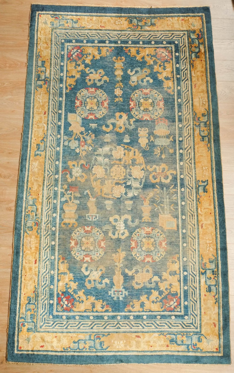May include: A vintage rug with a blue background and a yellow border. The rug features a repeating pattern of stylized flowers and geometric shapes.