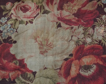 Può includere: Primo piano di un tessuto con un motivo floreale. Il tessuto presenta una varietà di fiori in tonalità di rosso, rosa e bianco, con foglie e steli verdi. Lo sfondo è di colore marrone scuro.