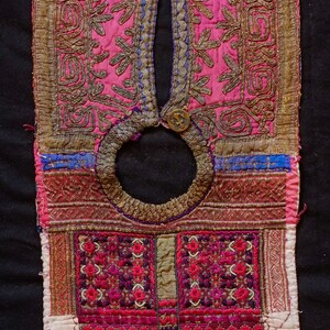 May include: A pink and gold embroidered fabric panel with a circular opening at the top. The panel is decorated with intricate floral and geometric patterns. The fabric is trimmed with a beaded border.