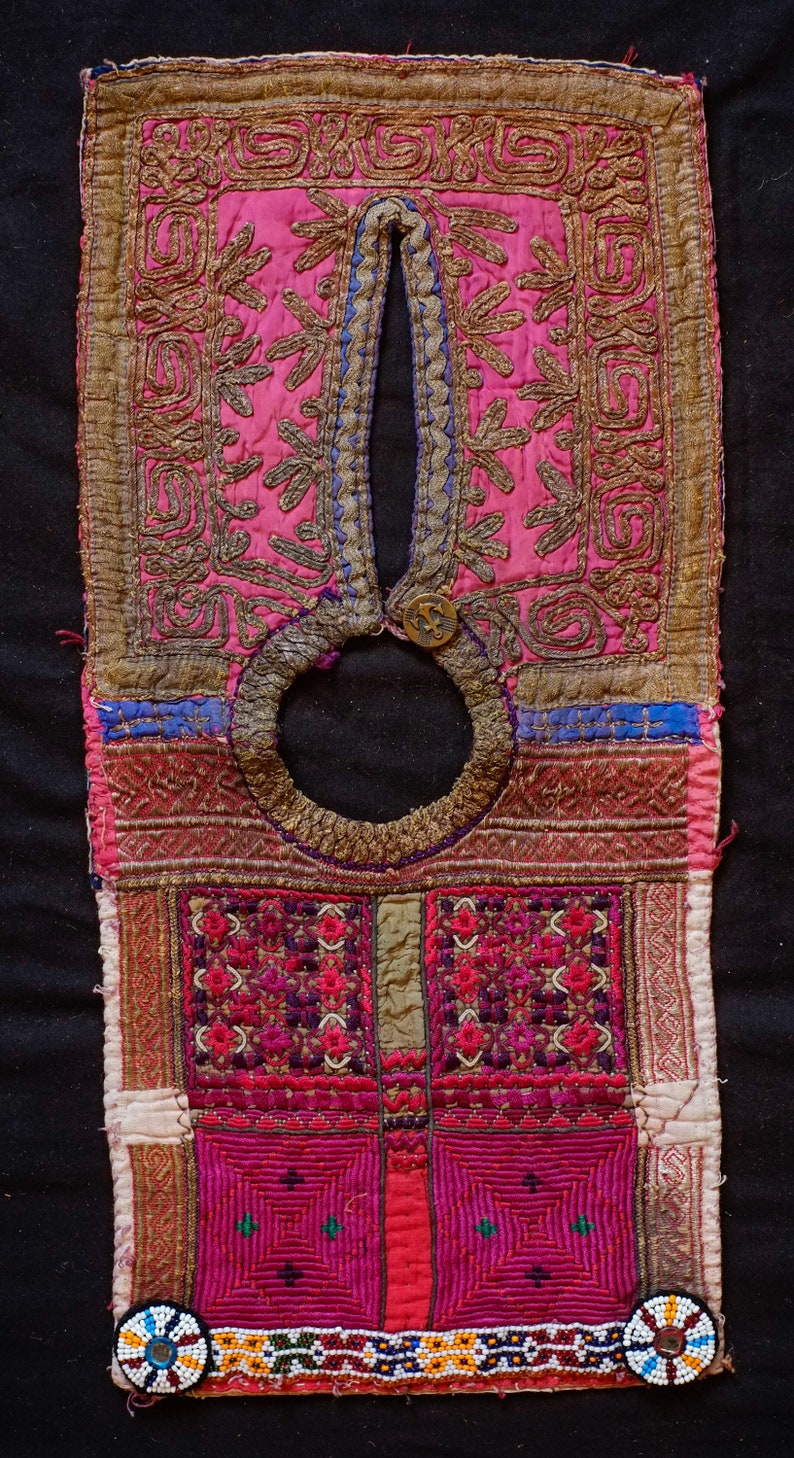 May include: A pink and gold embroidered fabric panel with a circular opening at the top. The panel is decorated with intricate floral and geometric patterns. The fabric is trimmed with a beaded border.