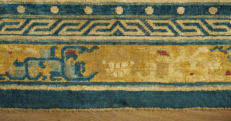 May include: Close-up of the bottom edge of a blue and yellow rug with a geometric pattern. The rug has a fringe border and is made of woven fabric.