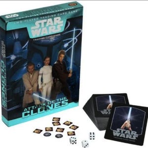 May include: A Star Wars: Attack of the Clones two-player trading card game box set. The box features images of characters with lightsabers. Includes a deck of cards, dice, and game tokens. The Star Wars logo is visible.
