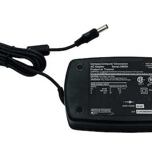 May include: A black Compaq AC adapter, Series 2862A, with a black power cord and connector. The adapter has text including "Compaq Computer Corporation" and "Product of Thailand".
