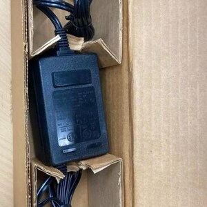 May include: A black power adapter with a cord and plug in a brown cardboard box.