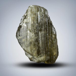 May include: A large, translucent, green and grey, rough-cut gemstone with striations.