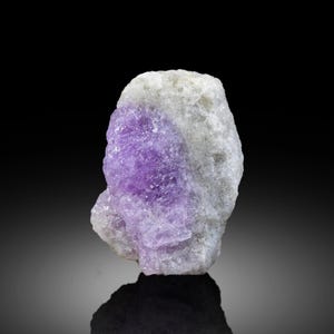 May include: A raw, natural amethyst crystal specimen. The stone features a vibrant purple hue contrasted against a white and gray matrix. The rough texture and color variations highlight its natural beauty, perfect for collectors or crystal enthusiasts.