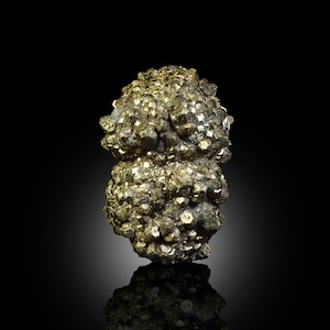 Può includere: Un gruppo di cristalli di pirite, nota anche come oro degli stolti, con un colore oro metallico. La formazione minerale ha una superficie ruvida e strutturata ed è posta su uno sfondo nero. I cristalli sono cubici e riflettono la luce.
