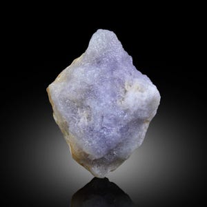 May include: A close-up of a rough, uncut, light purple crystal with a crystalline structure. The crystal has a pointed top and a rough, textured surface. The background is black, highlighting the crystal's color and form.