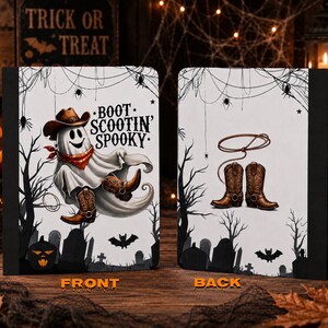 May include: A rectangular notebook with a white cover featuring a ghost wearing a cowboy hat, red bandana, and brown boots with the text BOOT SCOOTIN' SPOOKY on the front, and a lasso with brown cowboy boots on the back, set against a black graveyard.