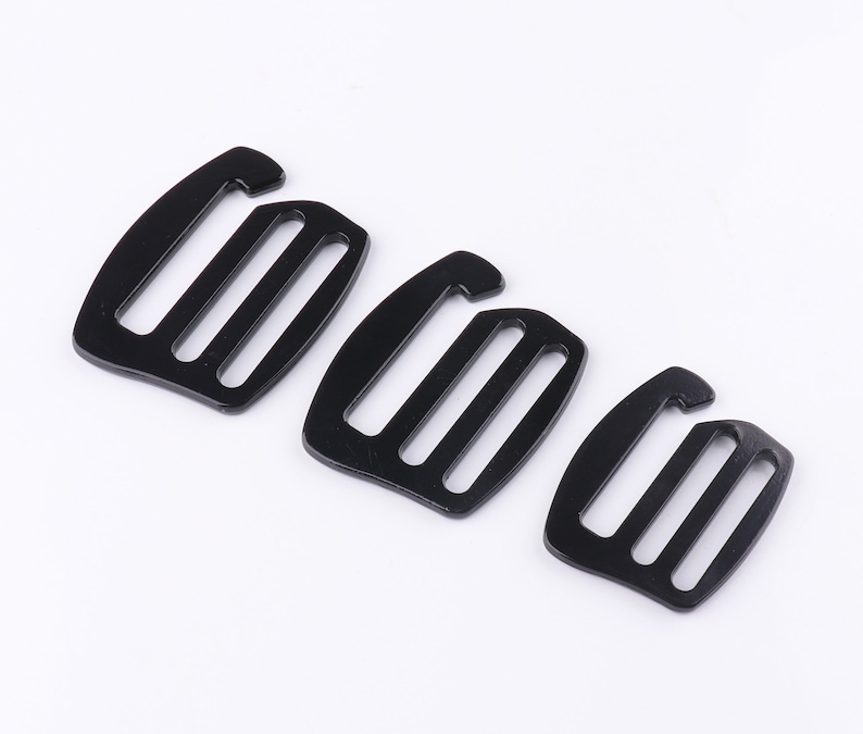 May include: Three black plastic slider buckles of different sizes. The buckles have three slots and are commonly used for straps, bags, and other DIY projects.