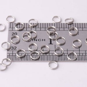 May include: A close-up of a ruler with silver jump rings scattered around it. The ruler is marked in inches and has a measurement of 1 inch and 2 inches.