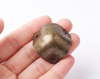 May include: A gold-toned metal corner protector with a rounded shape and three holes. The protector has a distressed finish.