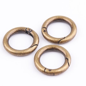 May include: Three antique gold-toned metal key rings with a spring-loaded clasp. The key rings are arranged in a triangular pattern on a white background.