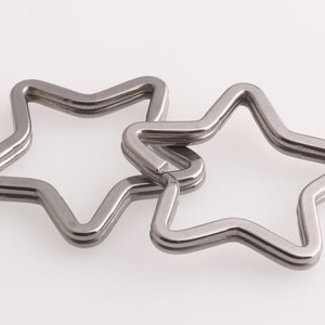 May include: Two silver star-shaped keychains, one slightly larger than the other, are linked together. The keychains are made of metal and have a smooth, polished finish.
