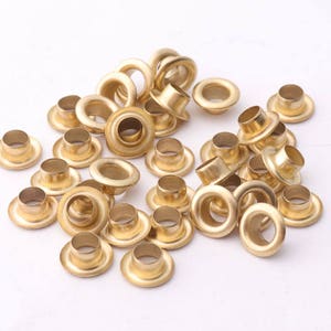 Puede incluir: Un montón de ojales de metal de color dorado, comúnmente utilizados para manualidades y trabajos en cuero.