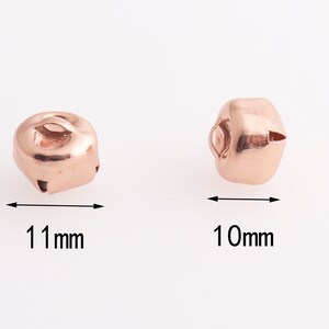 Może przedstawiać: Dwa dzwoneczki w kolorze r&oacute;żowego złota, jeden o wymiarach 11 mm, a drugi 10 mm.