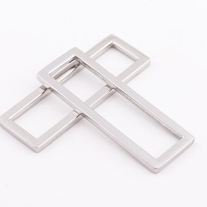 Puede incluir: Dos anillos rectangulares de metal plateado, uno ligeramente más grande que el otro, están apilados uno encima del otro.