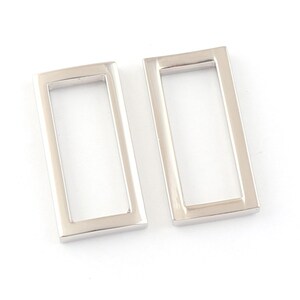 May include: Two silver metal rectangular frame shapes. The frames are hollow and have a smooth, polished finish.