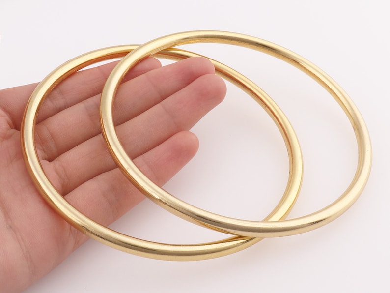 Op de afbeelding: Twee gouden metalen ringen, waarvan er &eacute;&eacute;n iets groter is dan de andere, worden getoond in een close-up afbeelding. De ringen zijn glad en glanzend.