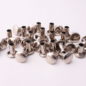 Peut inclure: Un tas de rivets en métal argenté, également appelés rivets creux ou œillets, avec une tête ronde et un cylindre creux. Ces rivets sont utilisés pour fixer du tissu, du cuir ou d'autres matériaux.