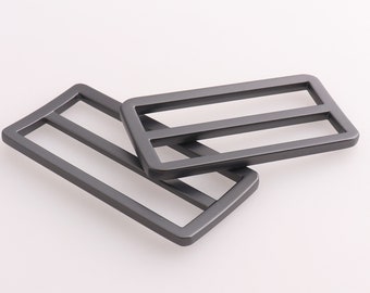 May include: Two black metal belt buckle slides with a rectangular shape and two horizontal lines.