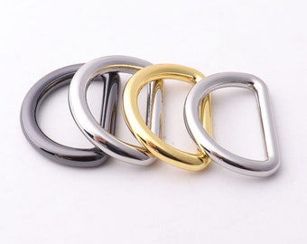 May include: Four metal D-rings in different finishes: black, silver, gold, and polished silver. The rings are stacked on top of each other.