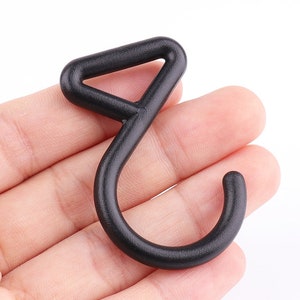 Puede incluir: Un gancho de plástico negro con una parte superior triangular. El gancho está diseñado para colgar objetos.