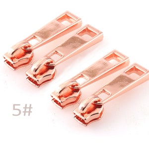 May include: Four rose gold zipper pulls with a 5# marking. The zipper pulls are rectangular with a small opening in the center.