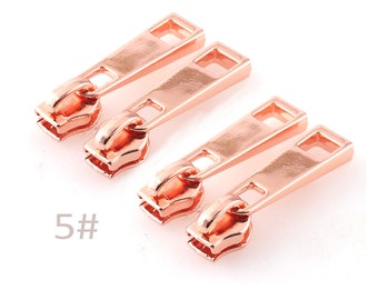 May include: Four rose gold zipper pulls with a 5# marking. The zipper pulls are rectangular with a small opening in the center.