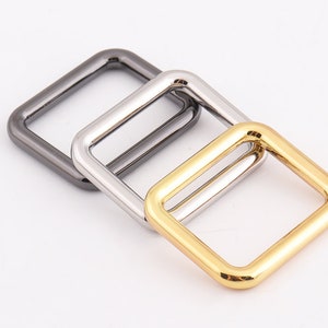 May include: Three metal square rings in different finishes: silver, gold, and black.