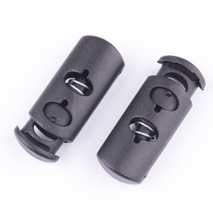 May include: Two black cord locks with a spring mechanism, designed to secure and adjust cords. The cord locks are made of durable plastic and are suitable for various applications.