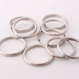 May include: A group of silver key rings, all of the same size and shape, are arranged in a pile on a white surface.