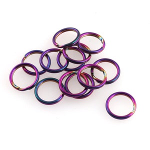 May include: A pile of 12 iridescent jump rings in shades of purple, blue, and green. The rings are made of metal and are approximately 2.5 cm in diameter.