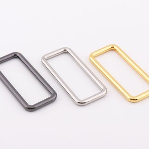 Pode incluir: Três anéis retangulares de metal em preto, prata e dourado.