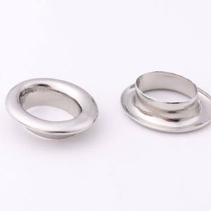 May include: Two silver metal eyelets, one with a raised lip and the other flat, for use in leather crafting or other DIY projects.