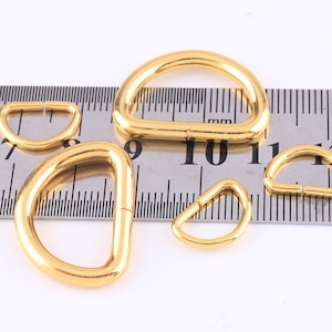 May include: Four gold-coloured metal D-rings of different sizes, measured against a ruler. The largest ring is approximately 2.5 cm in diameter.