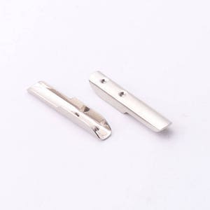 Puede incluir: Dos piezas de metal plateado con bordes redondeados y pequeños agujeros. Las piezas son planas y tienen una forma ligeramente curvada.