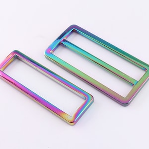 Pode incluir: Duas fivelas deslizantes retangulares de metal iridescente. A fivela maior mede aproximadamente 5 cm de comprimento e a fivela menor mede aproximadamente 2,5 cm de comprimento.